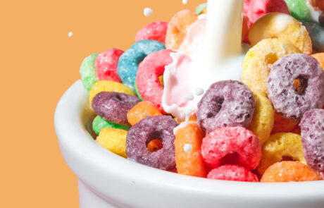 Milk pouring over Fruit Looks cereal in white bowl. Background is orange