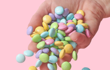 Pastel M&M's falling out of a white womans hand. The background is pink