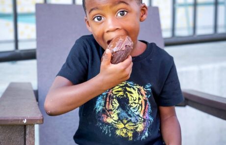 African American boy chomping down on a chocolate covered donut